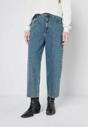 Helle blaue Jeans mit lässigem Schnitt, hoher Taille, subtiler Ausbleichung und klassischem Five-Pocket-Design, kombiniert mit schwarzen Stiefeletten.