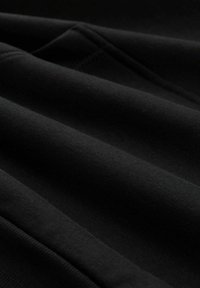 Schwarzer Stoff mit einer strukturierten Oberfläche, der Falten und Nähte aufweist. Das Material wirkt weich und hat eine einheitlich dunkle Farbgebung.