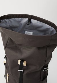 Roll-top ryggsekk laget av mørkeblå resirkulert stoff, med sølvfarget hardware, justerbare stropper og en teksturert overflate. Innvendig er den grå.