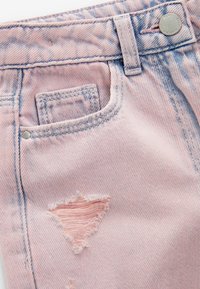 Gros plan sur la poche d'un jean en denim rose avec une boucle de ceinture, un rivet métallique, un bouton et une petite déchirure triangulaire usée sous la poche.