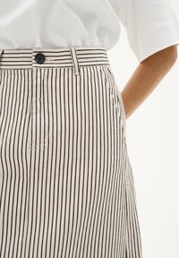 Jupe rayée avec des lignes verticales noires et crème, taille haute, fermeture à boutons et poches latérales. Fabriquée dans un tissu lisse avec une légère texture.