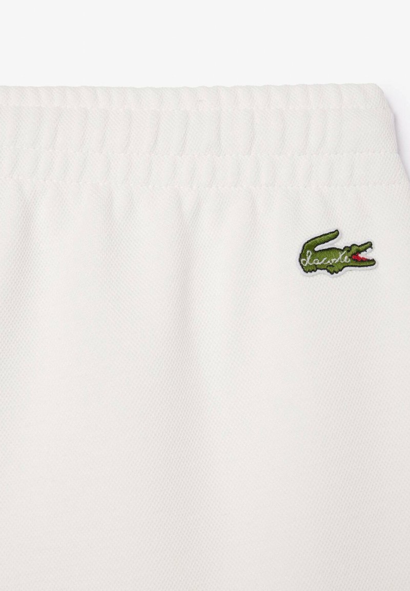 Shorts en tissu blanc avec une taille élastique et un petit logo crocodile brodé vert sur le côté gauche. Tissu texturé.