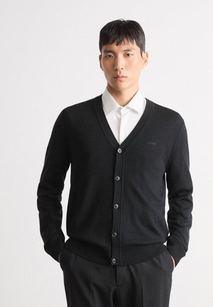 Cardigan negru din material tricotat, cu decolteu în V, manșete și tiv cu dantelă, și cinci butoane negre pe față. Logo subtil al mărcii.