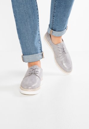 Chaussures grises à lacets en matériau texturé avec une finition brillante, dotées d'une semelle blanche et d'un accent en fibre naturelle autour de la semelle.