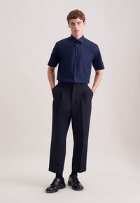 Marineblauw overhemd met korte mouwen met knopen, gecombineerd met marineblauwe hoge taille, wijde pijpen broek en zwarte veterschoenen, wat een strakke en moderne uitstraling geeft.