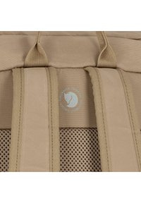 Zaino in tessuto beige con cinturini in tessuto e sezioni in rete, con un logo circolare che mostra il profilo di un animale bianco.