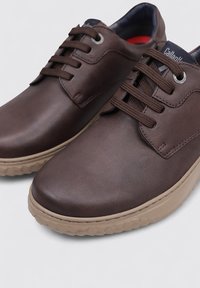 Chaussures en cuir marron avec une finition lisse, un bout rond et une semelle en caoutchouc beige épaisse ; elles comprennent des lacets ronds et des détails avec des œillets.