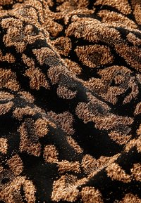 Černá látka s texturovaným vzorem zlatých leopardích skvrn, který má kovový lesk a jemnou, hladkou texturu.