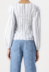 Blouse à rayures blanches et bleues avec un dos smocké, des manches bouffantes et un col rond ; associée à un jean bleu clair texturé avec un motif en losange.