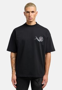 Sort bomulds t-shirt med korte ærmer, der har et farverigt broderet design på brystet. Løs pasform, rund halsudskæring og ensfarvet.