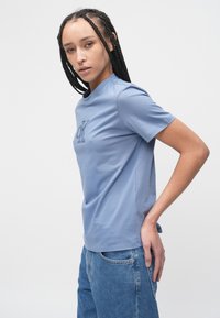 Lyseblå bomulls-t-skjorte med rund hals og korte ermer, med en subtil brodert logo foran. Kombinert med jeans.