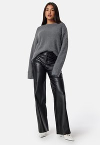 Maglione grigio fuzzy con maniche lunghe abbinato a pantaloni larghi neri in pelle sintetica. Il modello indossa tacchi a punta bianchi.