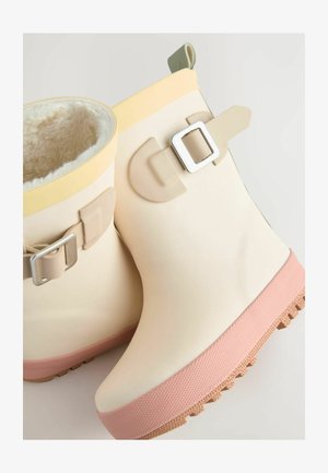 Šviesiai kreminiai guminiai kulkšnies batai su rožiniu tekstūruotu padu, su minkštu baltu pamušalu, geltonu apvadu ir sagtimi šone.