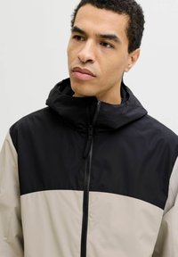 Veste zippée noire et beige avec capuche. Présente un design à blocs de couleur contrastée et un tissu léger et lisse.