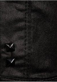 Svart denimkeps med två glänsande svarta pyramidhattar på sidan. Tyget har en slät yta med synliga sömmar.