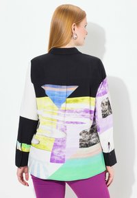 Chemise à boutons avec un col noir et des motifs géométriques colorés dans des nuances de violet, jaune, bleu et vert ; manches longues.