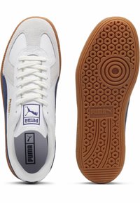 Weiße Sneaker aus Leder und dunkelblauem Wildleder mit flachen Schnürsenkeln, Gummisohle und kreisförmigem Muster. Puma-Logo auf der Zunge und Seite zu sehen.