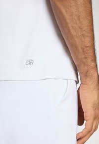 Witte sportieve t-shirt van textiel met een structuur, voorzien van een "ULTRA DRY" label aan de zoom. Het shirt is gecombineerd met witte shorts, die schone lijnen laten zien.