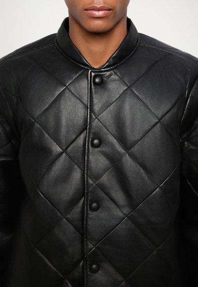Veste en cuir noir matelassée avec un col mandarin, un motif en losanges et des boutons ronds noirs sur le devant. Texture lisse.