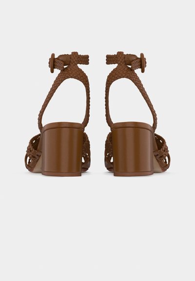 Καφέ σανδάλια με τακούνι τύπου block, πλεγμένα λουράκια στον αστράγαλο και κούμπωμα με αγκράφα, εμφανιζόμενα από πίσω σε λευκό φόντο.