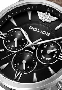 Montre à cadran noir avec des accents argentés, fonctions chronographe, grands index horaires et un logo POLICE bien visible avec un design ailé.