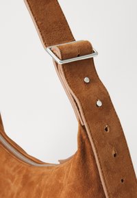 Borsa a spalla in suede marrone con superficie testurizzata, tracolla in pelle regolabile, accessori in argento e dettaglio con zip sul lato.