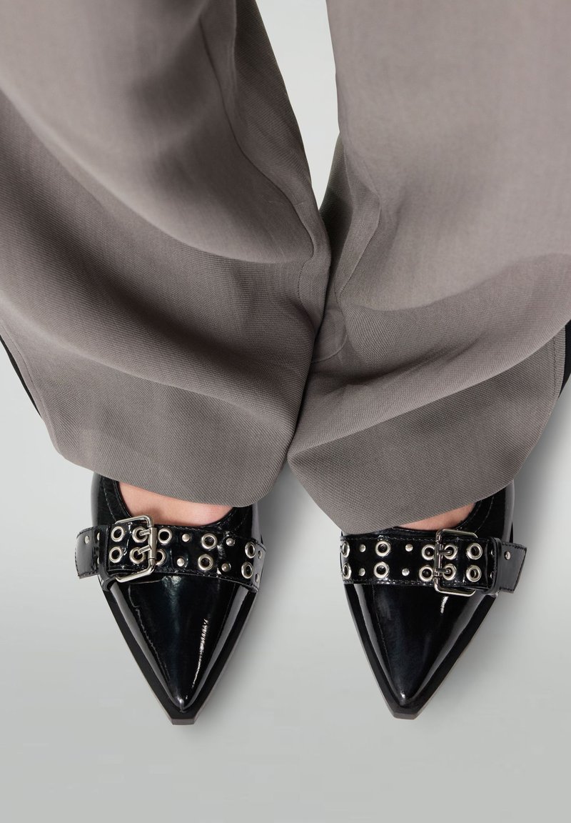 Zwarte gepatineerde leren schoenen met puntige neuzen en een glanzende afwerking, voorzien van een zwarte band versierd met zilveren oogjes en een metalen gesp.
