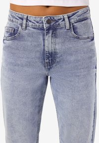 Ανοιχτό μπλε τζιν παντελόνι με ψηλή μέση, σχέδιο πέντε τσέπων και διακριτική φθορά. Διαθέτει κουμπί και φερμουάρ. Μέτριο βάρος υφάσματος.