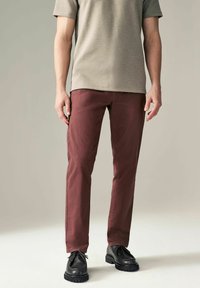 Pantalones de algodón burdeos con un ajuste Slim, combinados con una camisa gris de manga corta y zapatos de cuero negros con cordones y suelas texturizadas.