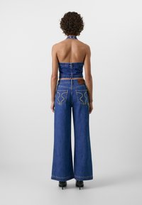 Denim halterneck top med en figursyet design og smocket ryg, parret med brede jeans med kontrastsying og baglommer.