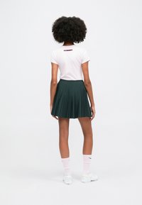 Rosa t-kreklu ar īsām piedurknēm un logo uz muguras, apvienota ar zaļu svārku ar krokām. Uzvilktas baltas kurpes un rozā zeķes.