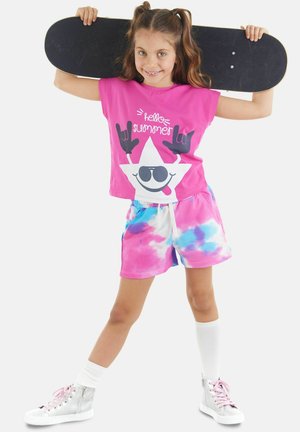 Camisa de manga corta rosa con un gráfico de una estrella sonriente, combinada con pantalones cortos de tie-dye multicolores en rosa, azul y blanco. Zapatillas de patinador.