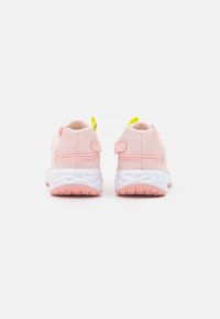 Scarpe da ginnastica rosa con una texture liscia, suola bianca e linguetta di richiamo gialla. Tacco arrotondato e dettagli di design minimalisti.