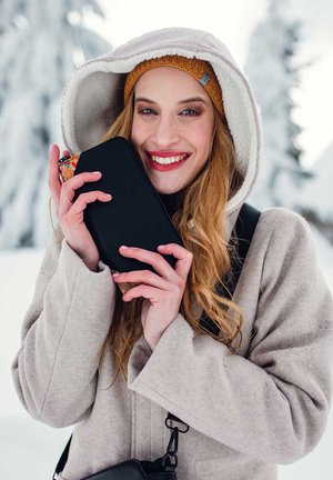Black zipper pouch held close, surrounded by a beige coat with fluffy hoodie lining. Soft, textured materials against a snowy background.