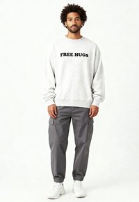 Sweat-shirt gris avec l'inscription "FREE HUGS" en lettres noires, accompagné d'un pantalon cargo gris et de baskets blanches. Tissu doux, coupe décontractée, poignets côtelés.