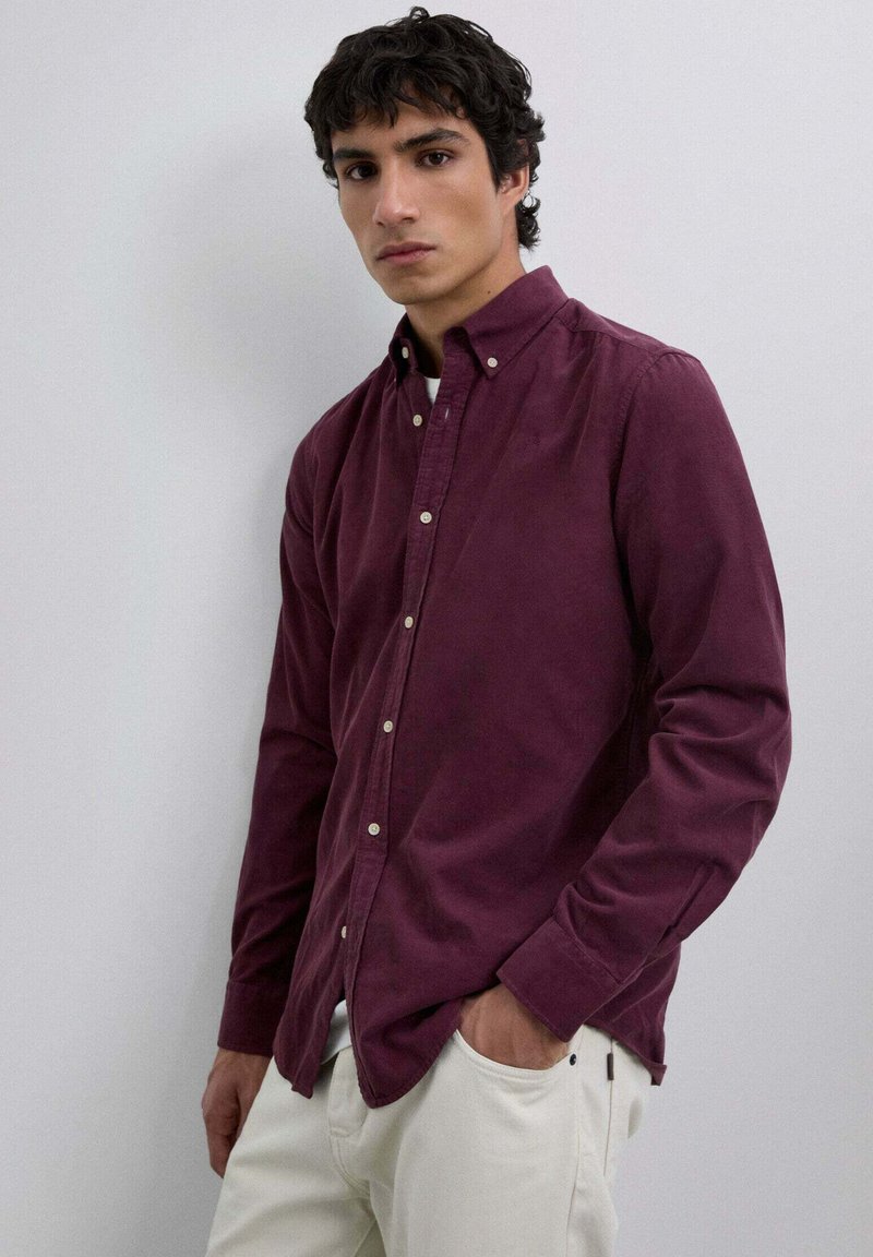 Weinrot button-down Hemd mit weicher Textur, langen Ärmeln und einem dezenten Kragen, kombiniert mit hellen Hosen. Glatte Oberfläche und maßgeschneiderte Passform.