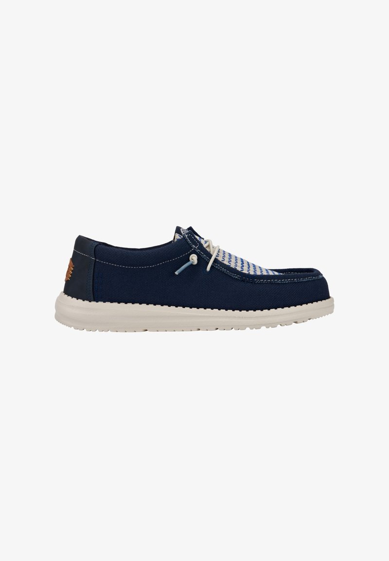 Scarpa in tela blu navy con suola in gomma bianca, caratterizzata da un design a righe sulla parte superiore e una sottile branding sul tallone. Chiusura con lacci.