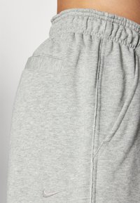 Calças de fato de algodão cinzentas com uma cintura elástica, bolso lateral e discreto logótipo da Nike. Tecido texturizado com um acabamento suave.