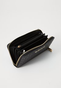 Black leather wallet with embossed pattern, gold zip closure, multiple compartments, and VALENTINO branding on the front.