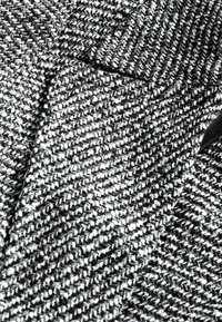 Tissu texturé en noir et blanc avec un motif tissé, présentant un design en chevrons avec des particules visibles et une apparence douce et chaleureuse.