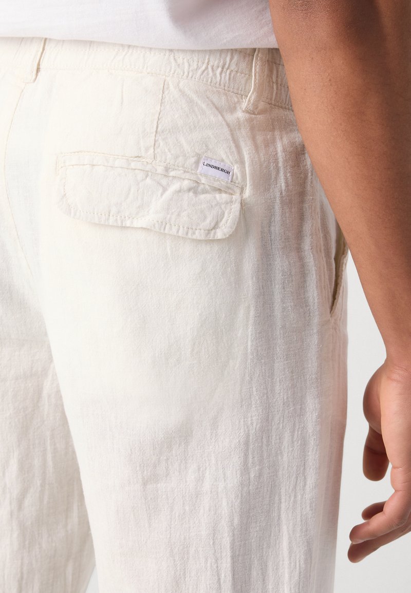 Pantalones blancos de lino con un acabado texturizado, bolsillos laterales y una etiqueta en el bolsillo trasero. Diseño casual con cinturilla elástica.