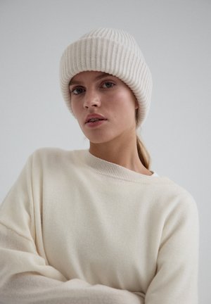 Kremowa, dziana czapka z prążkowanym wzorem oraz pasujący do niej kremowy, oversize'owy sweter. Wykonana z miękkich materiałów, o luźnym kroju i okrągłym dekolcie.