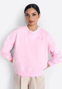 Felpa rosa con scollatura rotonda, spalle cadute e polsini a costine. Presenta un delicato motivo floreale sul petto. Materiale morbido.