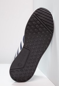 Svart sneaker sula med strukturerad hexagonal mönster, med vita ränder och varumärke. Gummimaterial, strukturerad design för grepp.
