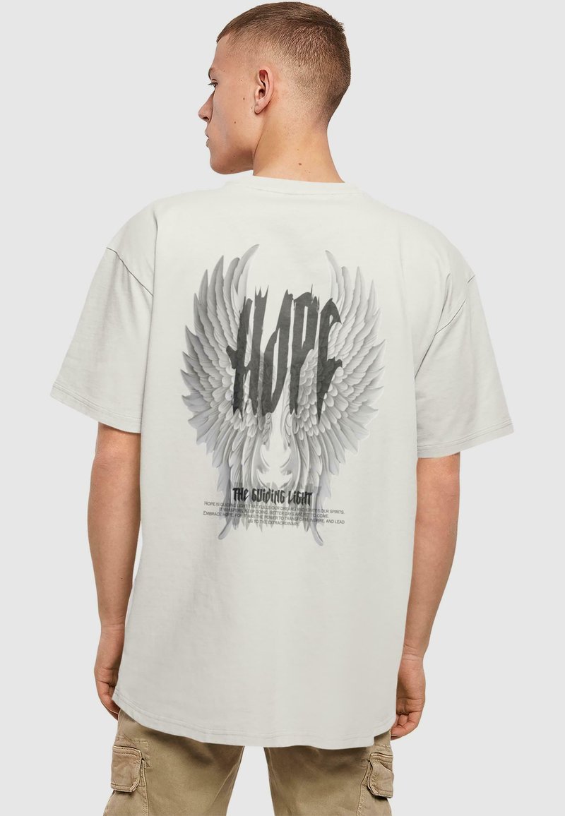 Lys grå oversized t-shirt med et stort sort-hvidt grafik af englevinger og teksten "HOPE" på ryggen.