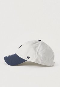 Άσπρο βαμβακερό καπελάκι μπέιζμπολ με σκουρομπλε γείσο, διακοσμημένο με κεντημένα λογότυπα και ρυθμιζόμενο λουράκι στο πίσω μέρος.