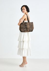 Sac fourre-tout en imprimé léopard avec deux poches avant, une poignée supérieure et un détail de boucle, associé à une robe blanche à volants et des chaussures à lanières.