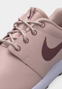 Rosa Ledersneaker mit mauvefarbenem Nike-Swoosh, passenden Ösen und Schnürsenkeln auf weißer Sohle, die Textur und Nahaufnahme der Nähte hervorhebt.