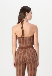 Brun mönstrad crop top med halterneck-design, med en texturerad yta och en figurnära silhuett. Bakifrån syns knutna band.
