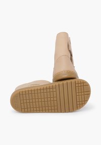 Beżowe skórzane botki z teksturowaną gumową podeszwą i starannym przeszyciem. Zapięcie na rzep z boku ułatwiające zakładanie.